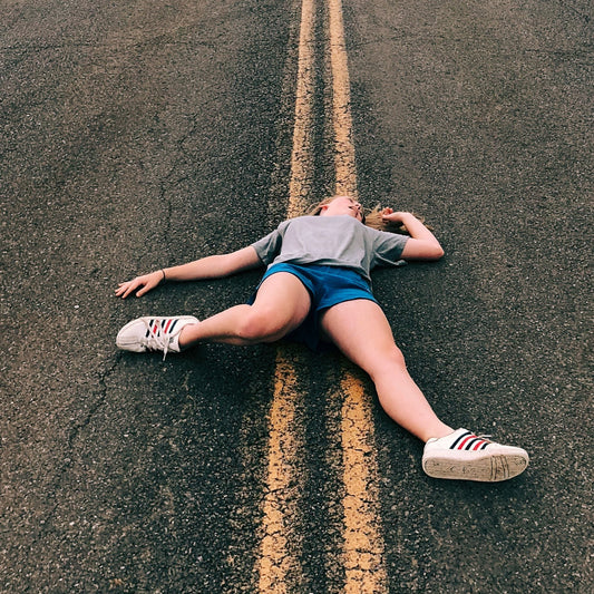 Exhausted female runner lie down on the road, sweaty shoes — illustrates running fatigue, post-run recovery, hydration and rest tips.