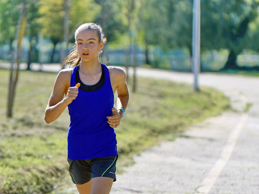Woman runner hydrating with water bottle during hot summer run, wearing hydration vest and sports gear, staying cool and hydrated while marathon training in the heat.