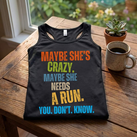 A black racerback tank top with a colorful retro-style text graphic reading 'MAYBE SHE'S CRAZY. MAYBE SHE NEEDS A RUN.