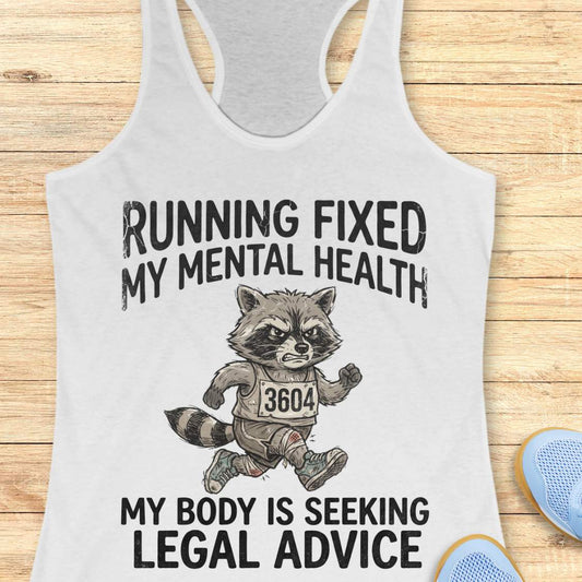 A white racerback tank top laid flat on a light wood background, featuring a printed graphic of a raccoon runner with the text 'RUNNING FIXED MY MENTAL HEALTH MY BODY IS SEEKING LEGAL ADVICE'. Partial blue shoes are visible at the bottom right as styling props.