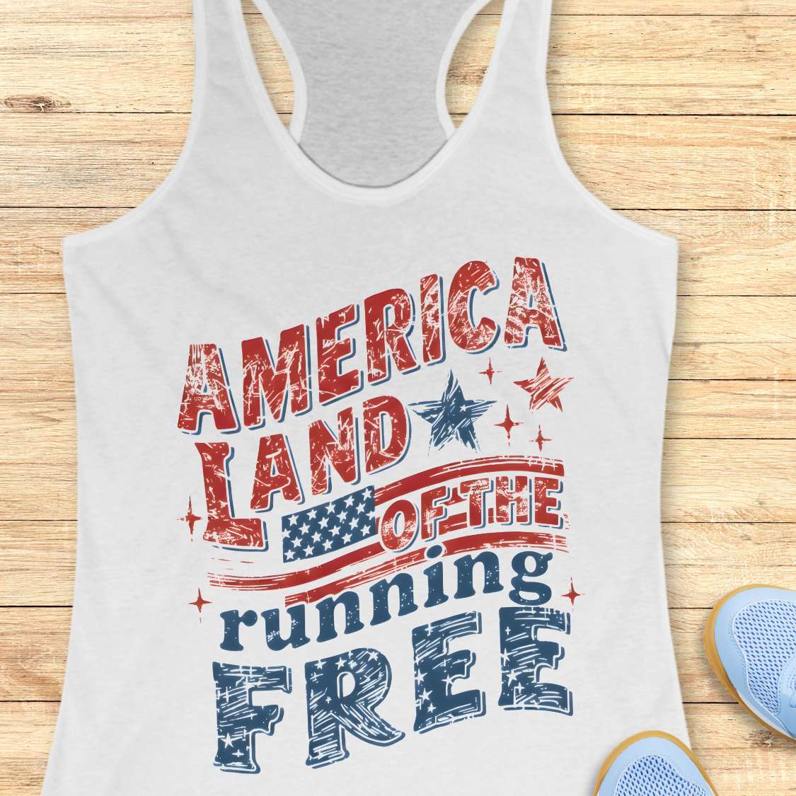 White tank top with 'America Land of the running Free' text and American flag design on a wooden surface.
