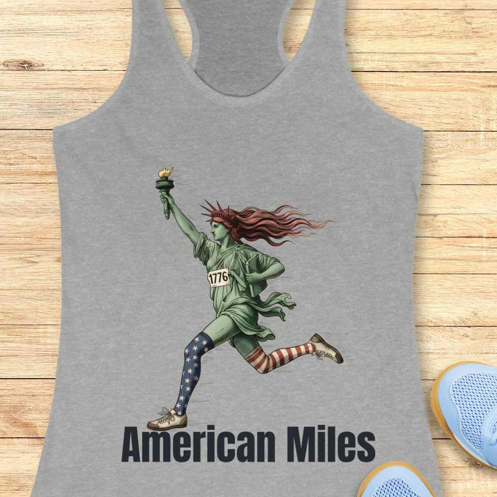 Graphic design on a gray tank top depicting a running Statue of Liberty with vibrant red hair, a 1776 race bib, mismatched star-and-stripe patterned socks, and American Miles text