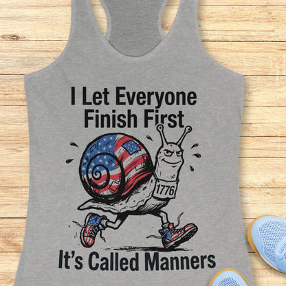 Gray tank top with a snail graphic and text  I let everyone finish first it's called manners,  on a wooden surface