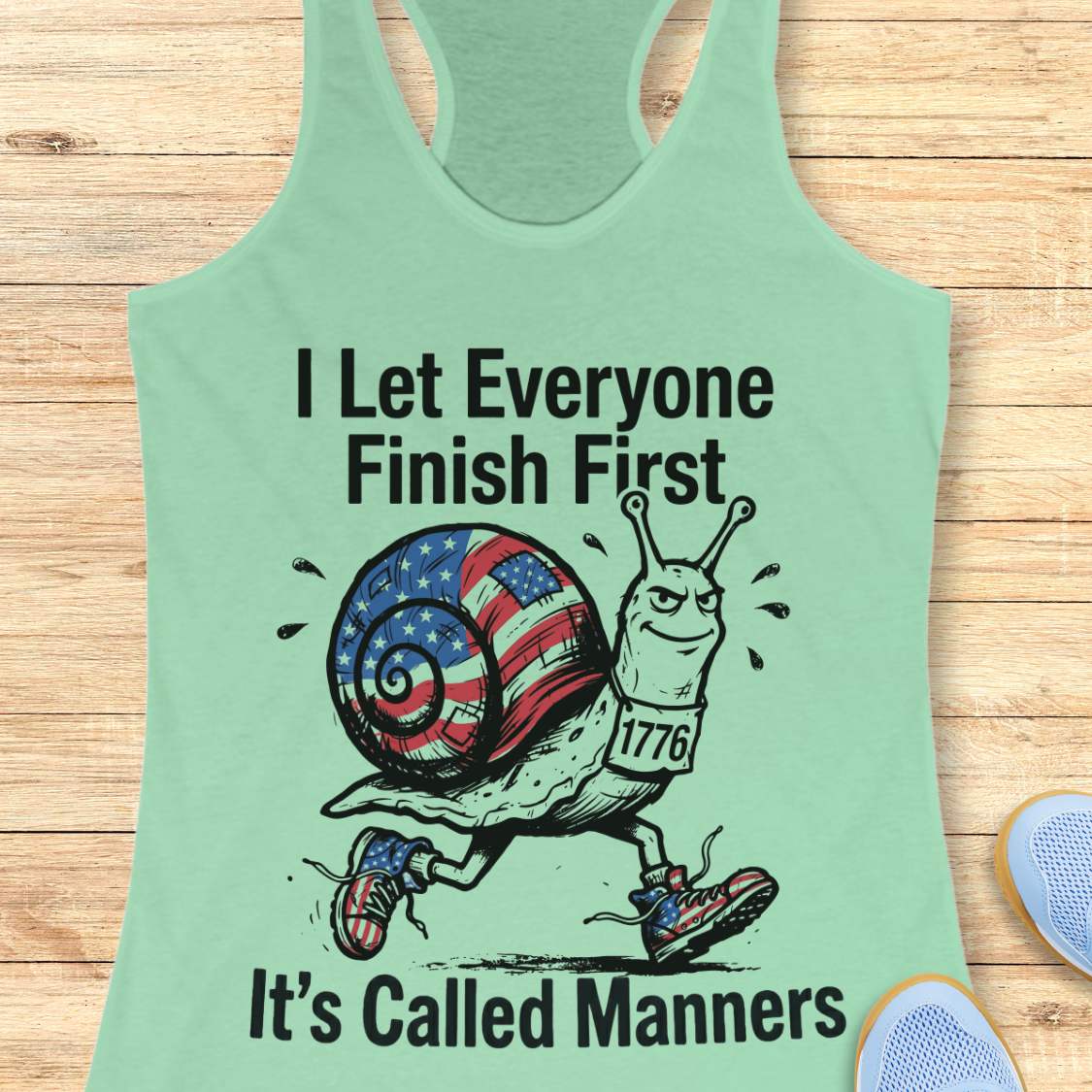 Mint green tank top with a snail graphic and text  I let everyone finish first it's called manners,  on a wooden surface