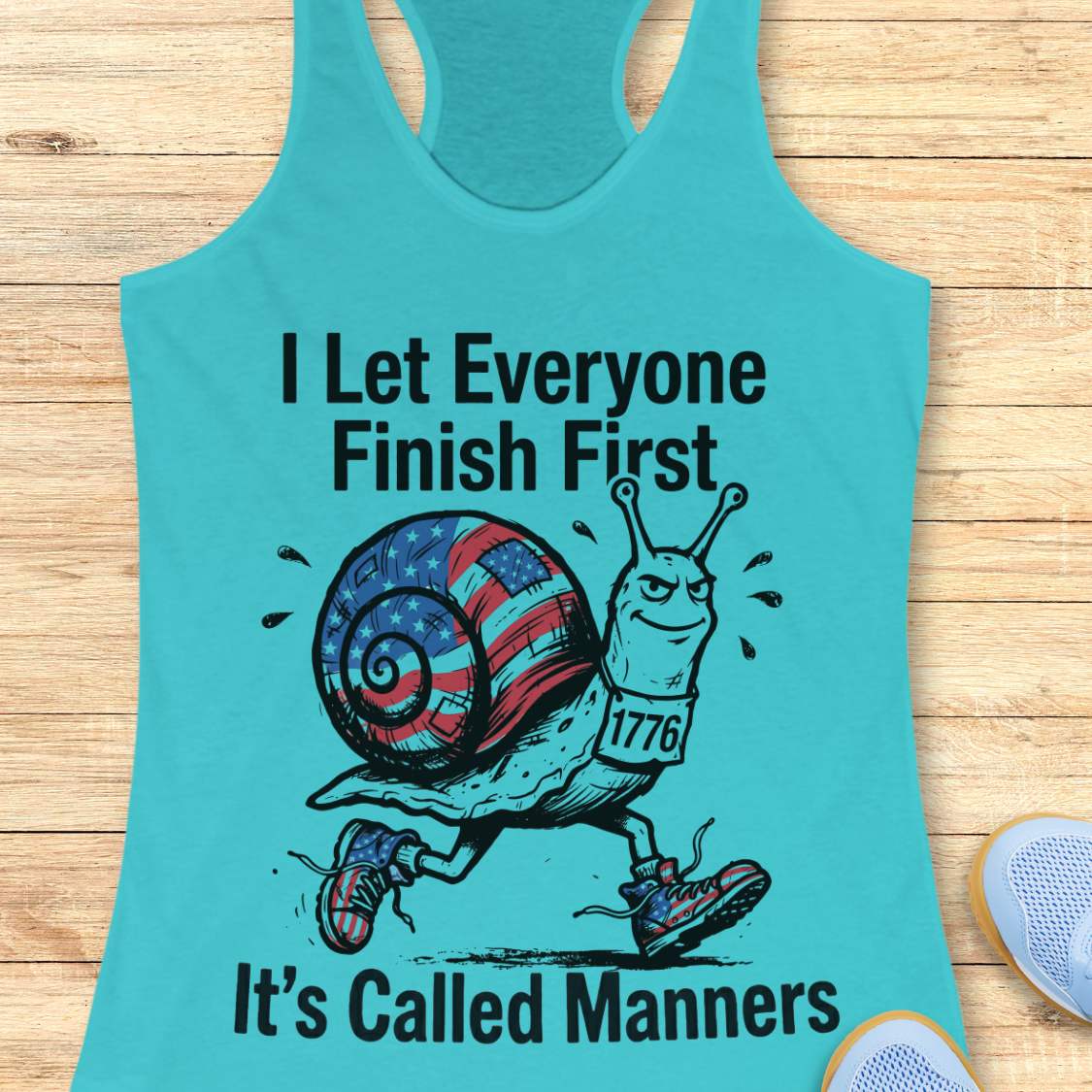 Turquoise tank top with a snail graphic and text  I let everyone finish first it's called manners, on a wooden surface