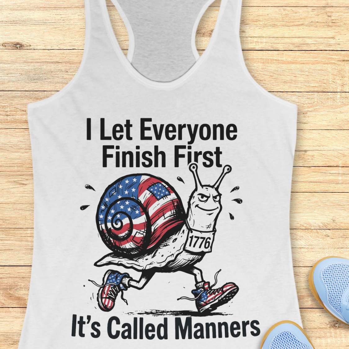 white tank top with a snail graphic and text  I let everyone finish first it's called manners, on a wooden surface