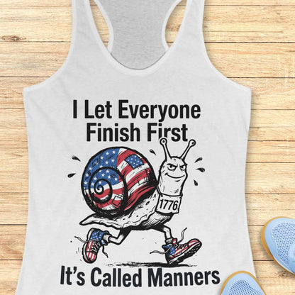 white tank top with a snail graphic and text  I let everyone finish first it's called manners, on a wooden surface
