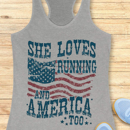 Gray tank top with 'She Loves Running and America Too' text and American flag design on a wooden surface.