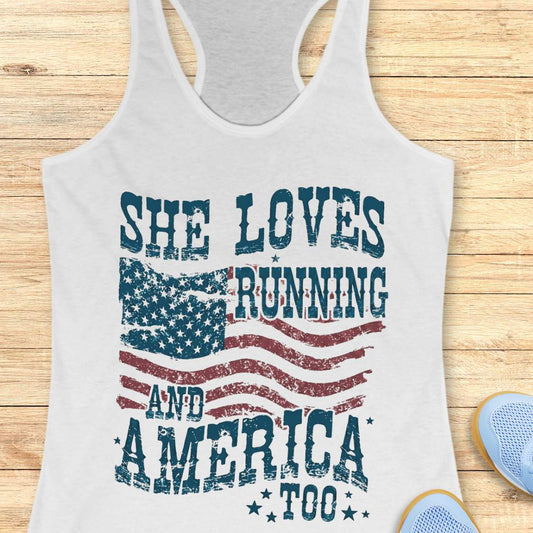 white tank top with 'She Loves Running and America Too' text and American flag design on a wooden surface.