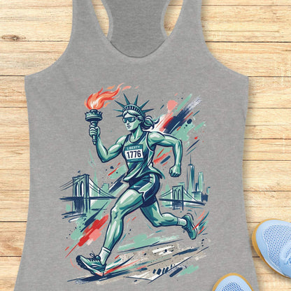 Gray tank top with a graphic of a running Lady Liberty  holding a torch on a wooden surface