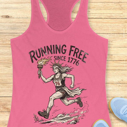 pink tank top with a design of lady liberty running and text - 'running free since 1776', on a wooden surface.