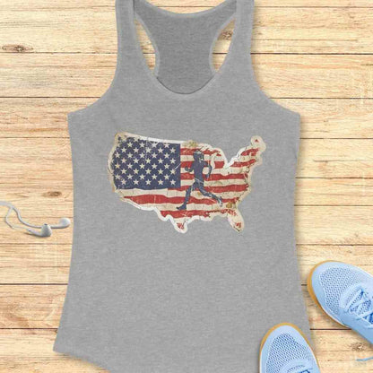 Grey racerback tank top featuring a distressed American flag map with a dark blue runner silhouette, displayed on a wooden background with light blue athletic shoes and white earbuds