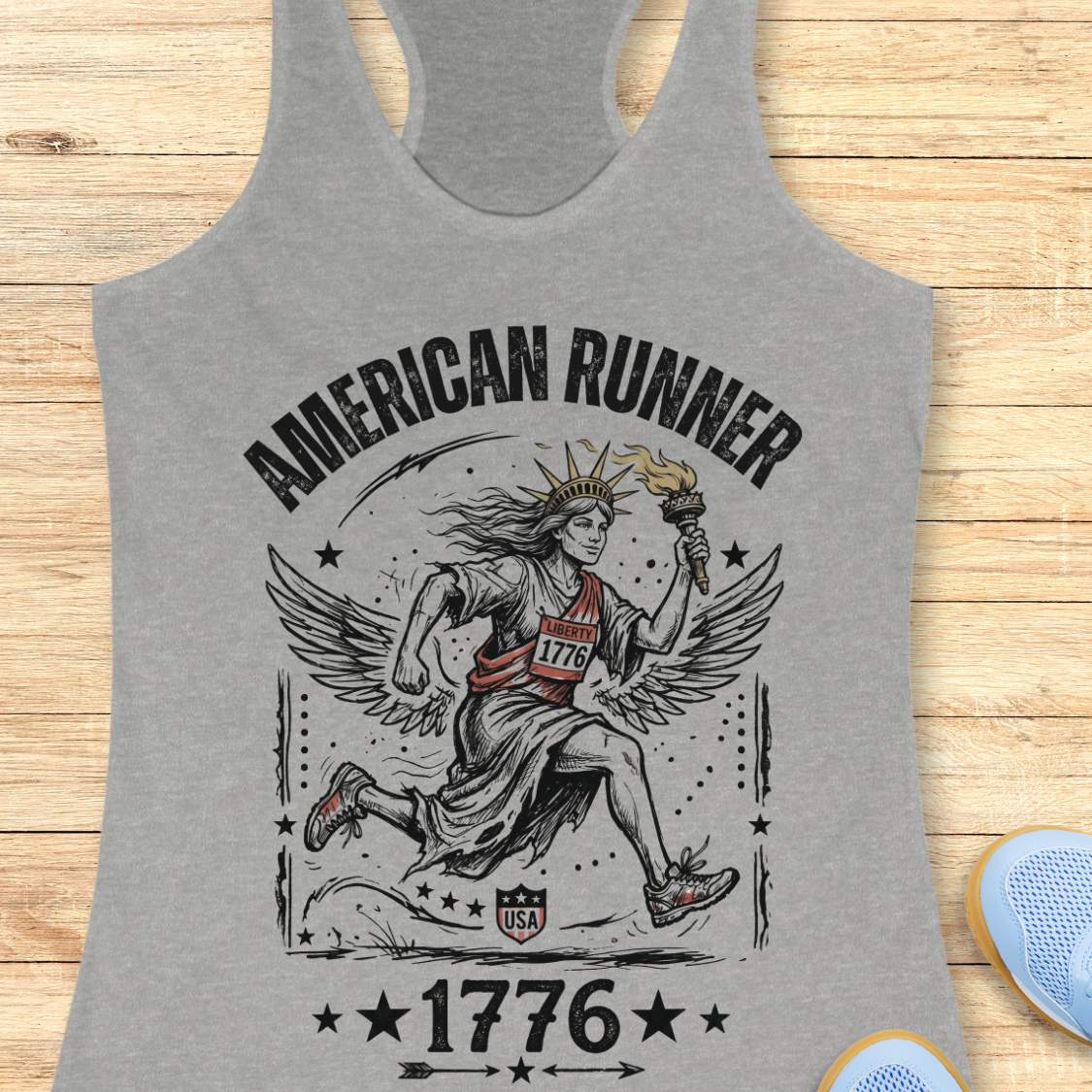 grey tank top with a design of lady liberty running and text - 'American runner 1776', on a wooden surface.