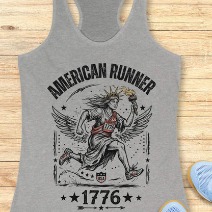 grey tank top with a design of lady liberty running and text - 'American runner 1776', on a wooden surface.