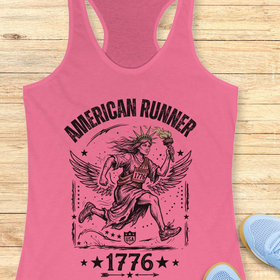 pink tank top with a design of lady liberty running and text - 'American runner 1776', on a wooden surface.