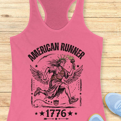 pink tank top with a design of lady liberty running and text - 'American runner 1776', on a wooden surface.