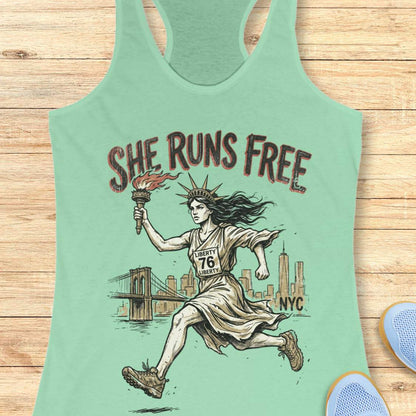 mint tank top with a design of lady liberty running and text - 'she runs free NYC', on a wooden surface.