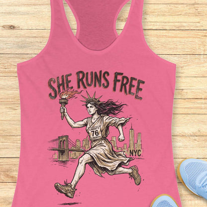 pink tank top with a design of lady liberty running and text - 'she runs free NYC', on a wooden surface.
