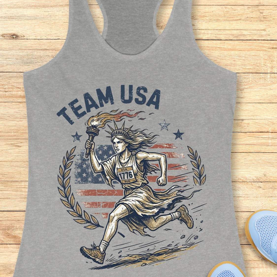 Gray tank top with 'Team USA' design featuring lady liberty running and American flag on a wooden surface.