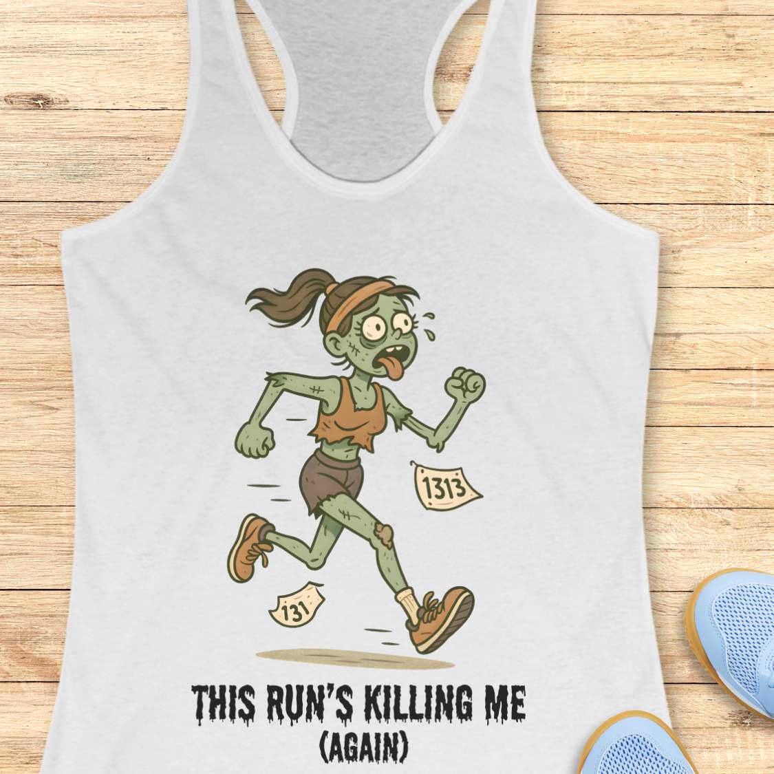 White racerback tank top displaying a humorous cartoon zombie runner with green skin, tattered brown clothes, race bibs 131 and 1313, and the slogan 'THIS RUN'S KILLING ME (AGAIN)' set against a light wooden background with partial blue running shoes and white earbuds visible