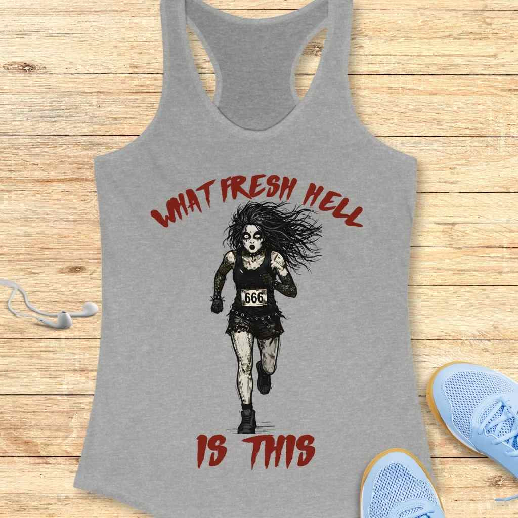 A gray tank top featuring a graphic print of a pale gothic runner with dark eye makeup, wild black hair, wearing a black tank top and ripped skirt with a "666" race bib, alongside red distressed text "WHAT FRESH HELL IS THIS", displayed on a wooden surface with light blue sneakers and white earbuds