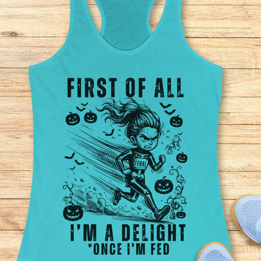 A turquoise racerback tank top laid flat on a light wood surface, featuring a black graphic of a woman running with pumpkins, bats, and the text 'FIRST OF ALL I'M A DELIGHT *ONCE I'M FED'. Part of a white shoe is visible at the bottom right.