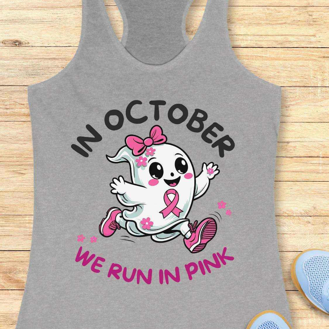 grey tank top with a cartoon ghost and pink ribbon design with the text - 'in October we run in pink', on a wooden surface.