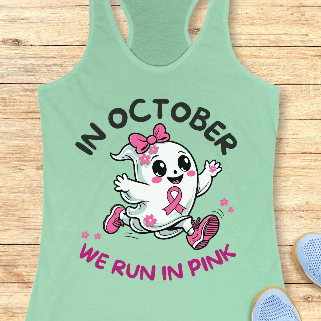 mint tank top with a cartoon ghost and pink ribbon design with the text - 'in October we run in pink', on a wooden surface.