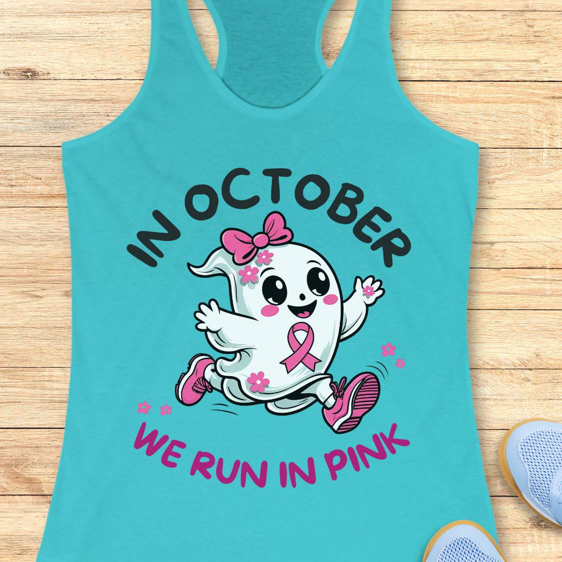blue tank top with a cartoon ghost and pink ribbon design with the text - 'in October we run in pink', on a wooden surface.