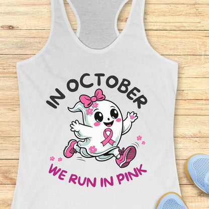 white tank top with a cartoon ghost and pink ribbon design with the text - 'in October we run in pink', on a wooden surface.