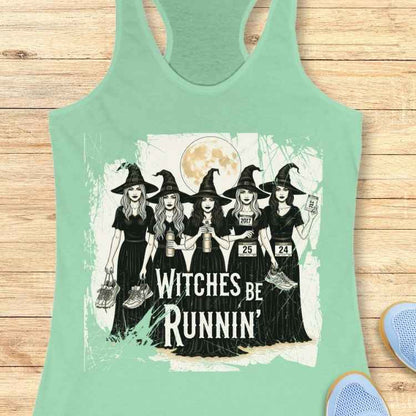 Graphic design on a mint green tank top depicting five cartoon witches in black dresses and pointy hats under a full moon, holding running shoes and water bottles with race bibs, above the text "WITCHES BE RUNNIN'"