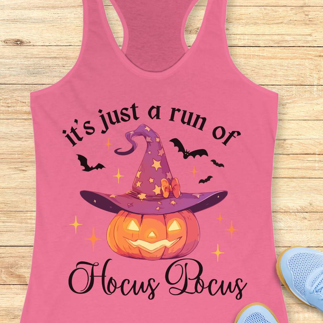pink tank top with Halloween design featuring a pumpkin and witch hat on a wooden surface.