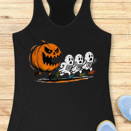 Black racerback tank top featuring a Halloween running graphic of an angry orange jack-o'-lantern chasing three white ghosts wearing numbered race bibs 101 56 and 32 with colorful blue green and orange running shoes displayed on a light wooden background alongside white earbuds and light blue sneakers