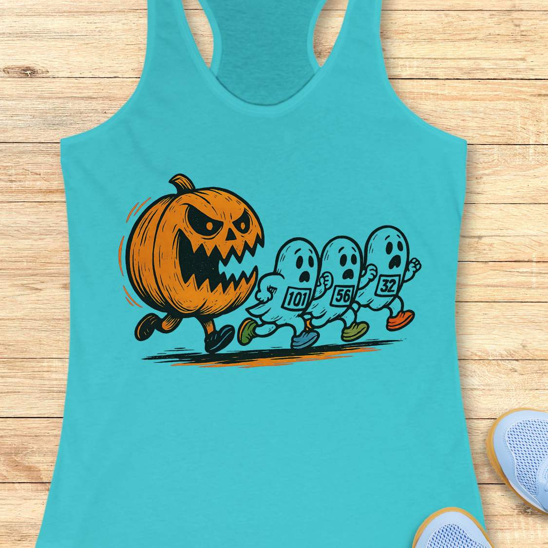 blue racerback tank top featuring a Halloween running graphic of an angry orange jack-o'-lantern chasing three white ghosts wearing numbered race bibs 101 56 and 32 with colorful blue green and orange running shoes displayed on a light wooden background alongside white earbuds and light blue sneakers