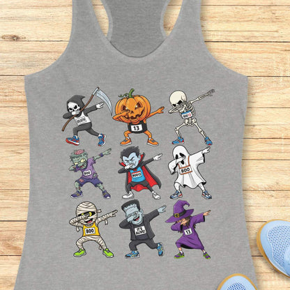 Digital illustration on a grey racerback tank top showcasing nine dabbing Halloween cartoon characters including a Grim Reaper, pumpkin, skeleton, zombie, vampire, ghost, mummy, Frankenstein's monster, and a witch, many wearing race bibs like 'DEATH' or 'BOO,' displayed on a rustic wooden background with blue sneakers and white earbuds nearby