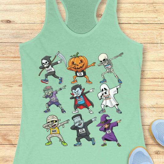 Digital illustration on a light mint green racerback tank top showcasing nine dabbing Halloween cartoon characters including a Grim Reaper, pumpkin, skeleton, zombie, vampire, ghost, mummy, Frankenstein's monster, and a witch, many wearing race bibs like 'DEATH' or 'BOO,' displayed on a rustic wooden background with blue sneakers and white earbuds nearby