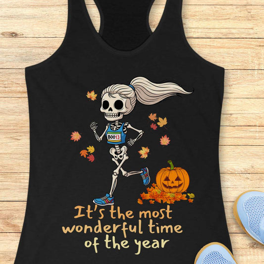 Graphic design on a black tank top features a female skeleton with a ponytail wearing a blue running bib B0013 and blue sneakers, running past a smiling jack-o'-lantern and colorful autumn leaves, with the text It's the most wonderful time of the year