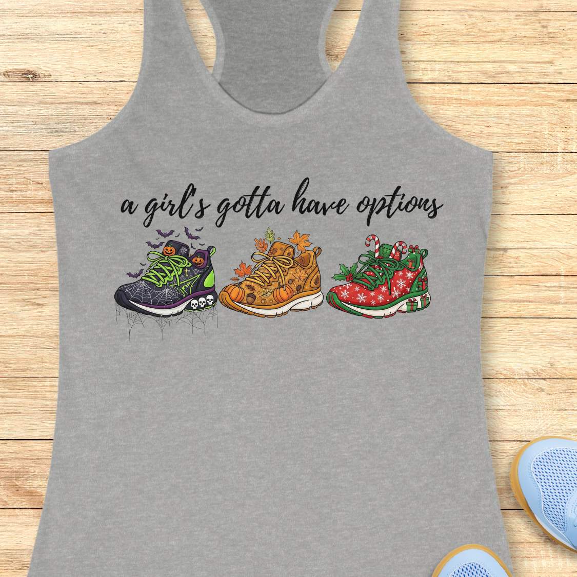 grey tank top with running shoes designs and text 'a girl's gotta have options',  on a wooden surface