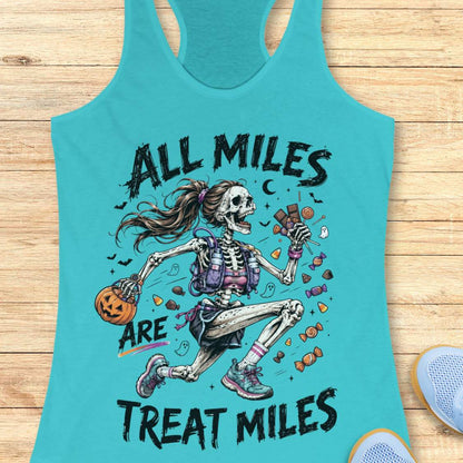 A turquoise racerback tank top laid flat on a light wood surface, featuring a colorful Halloween graphic of a skeleton girl holding a pumpkin and candy, with the text 'ALL MILES ARE TREAT MILES'. A partial blue shoe is visible at the bottom right.