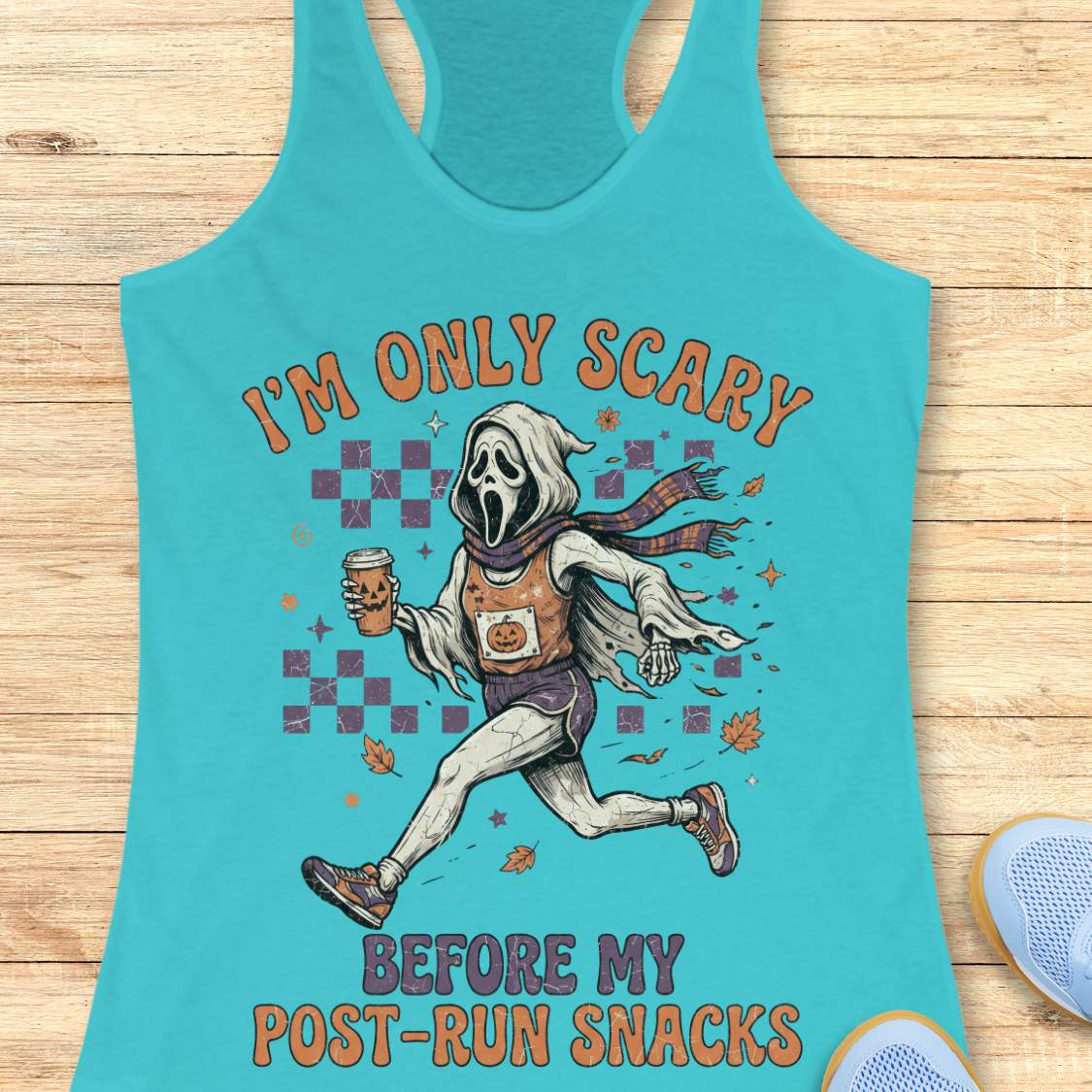 A turquoise racerback tank top laid flat on a light wood surface, featuring a humorous graphic of a Ghostface-like running ghost holding a beer can with the text 'I'M ONLY SCARY BEFORE MY POST-RUN SNACKS'.