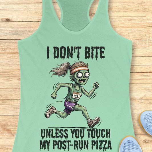 A mint green racerback tank top laid flat on a light wood background, featuring a cartoon zombie runner graphic with the text 'I DON'T BITE UNLESS YOU TOUCH MY POST-RUN PIZZA.' A blue shoe is partially visible at the bottom right as a styling prop.