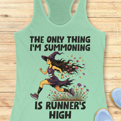 A mint racerback tank top laid flat on a light wood surface, featuring a Halloween graphic of a witch running with a text 'The only thing I'm summoning is runner's high'.