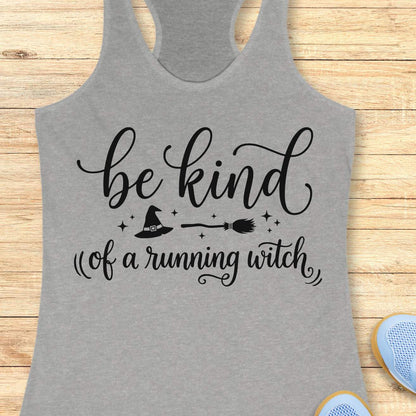 A heather gray racerback tank top with a black graphic print that reads 'be kind of a running witch' with a witch hat and broomstick illustration, laid flat on a light wood background.