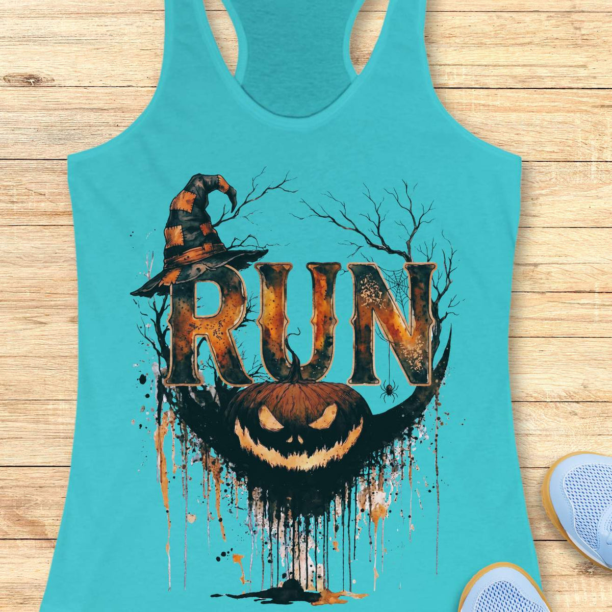 blue racerback tank top featuring a Halloween-themed running design. The graphic displays the word “RUN” in large distressed orange and black letters, topped with a weathered witch hat. Behind the text are bare tree branches, a spider web, and a hanging spider. A grinning jack-o'-lantern with dripping black and orange paint effects sits below the lettering, creating a spooky autumn aesthetic. The tank top is displayed on a light wooden background with partial blue running shoes visible in the corners.