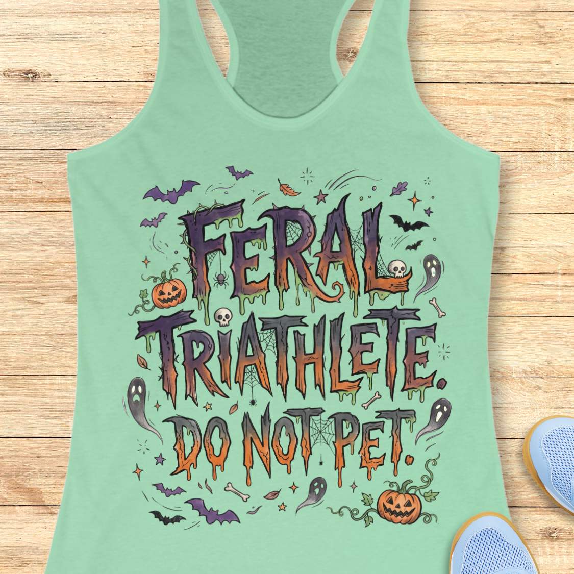 Funny Halloween running mint tank top featuring the slogan “Feral Triathlete Do Not Pet” in spooky dripping typography surrounded by bats, ghosts, pumpkins, spider webs, and Halloween elements. Humorous athletic apparel for women runners, triathletes, marathoners, and Halloween race participants.