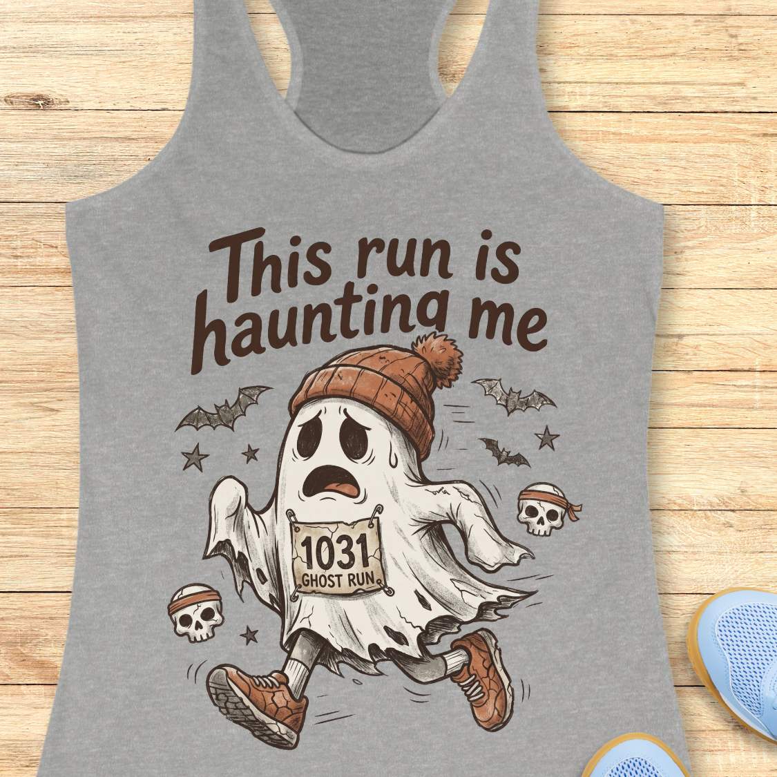 grey Halloween tank top with an image of a running ghost and text 'This run is haunting me', on a wooden surface