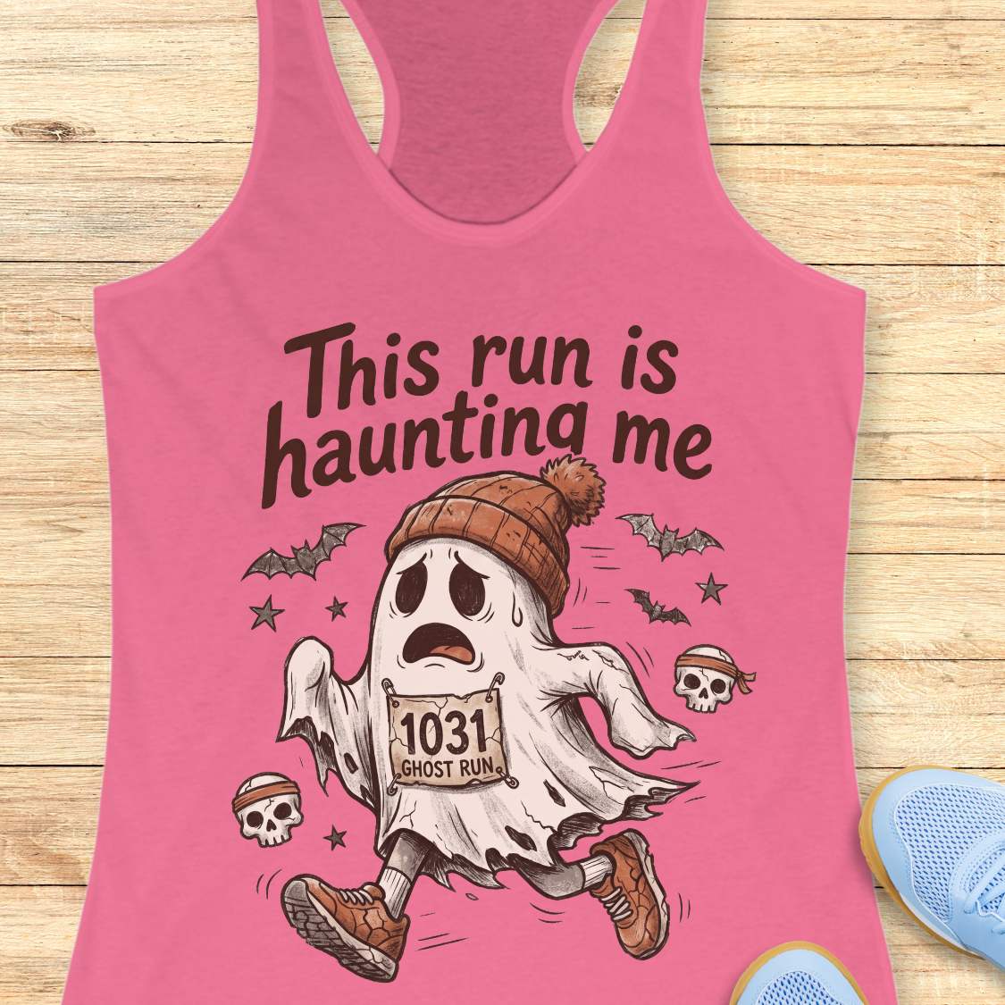 pink Halloween tank top with an image of a running ghost and text 'This run is haunting me', on a wooden surface