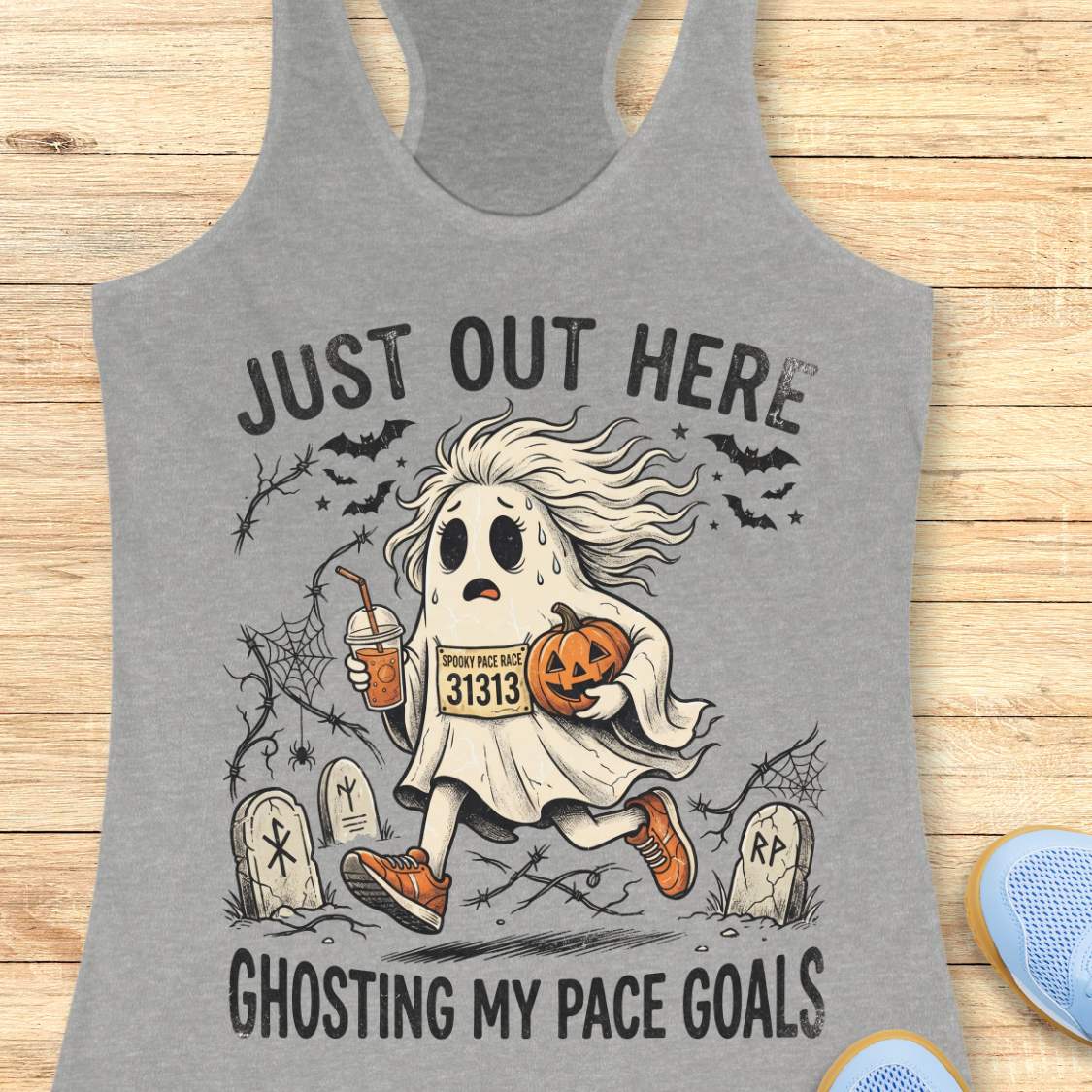 grey Halloween tank top with an image of a running ghost and text 'Just out here ghosting my pace goals', on a wooden surface
