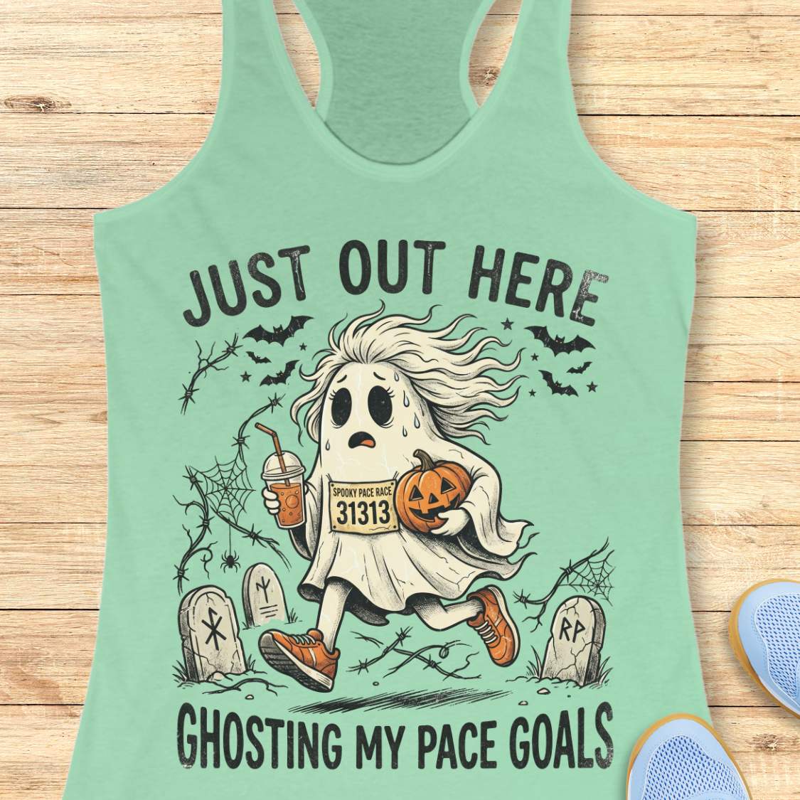mint Halloween tank top with an image of a running ghost and text 'Just out here ghosting my pace goals', on a wooden surface