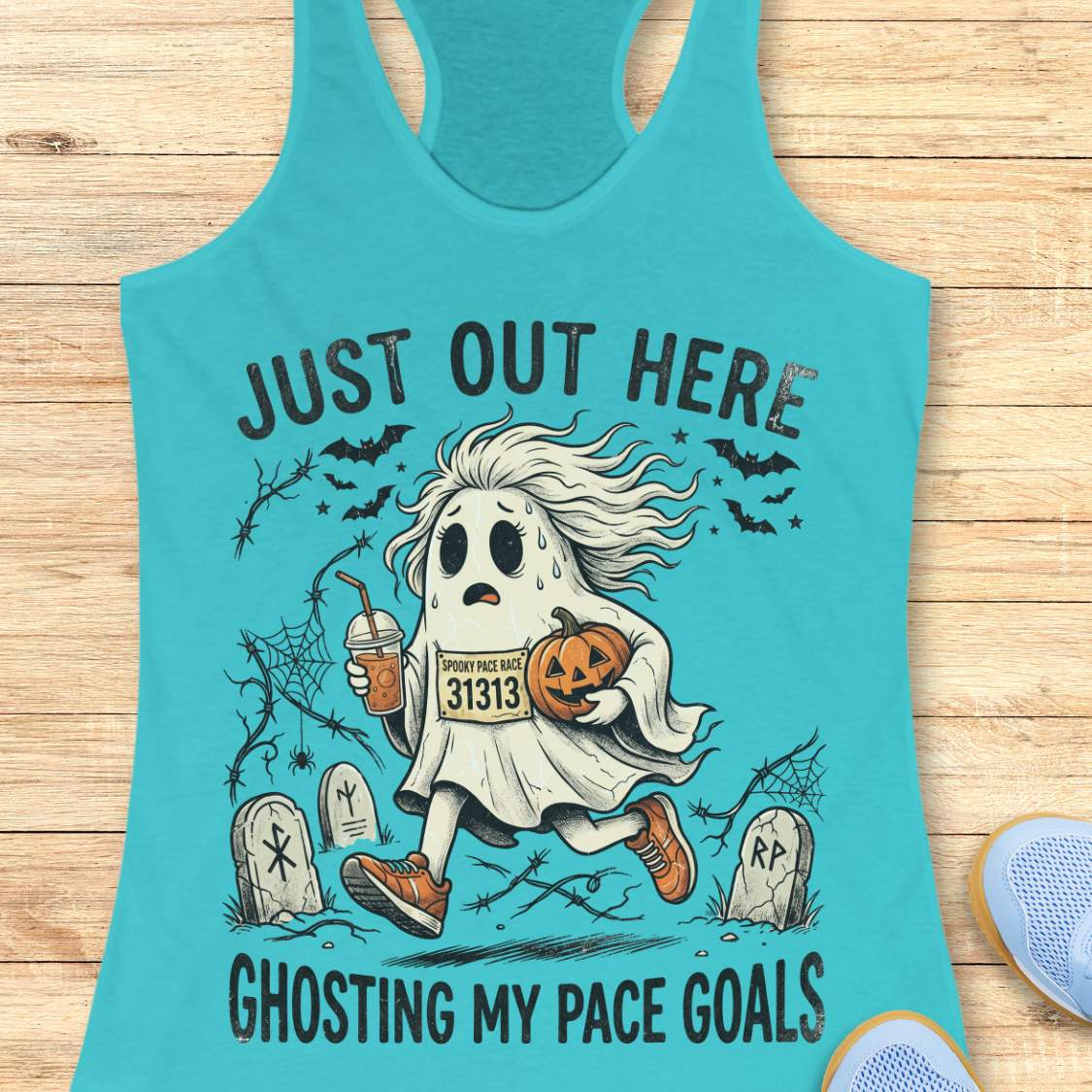 blue Halloween tank top with an image of a running ghost and text 'Just out here ghosting my pace goals', on a wooden surface